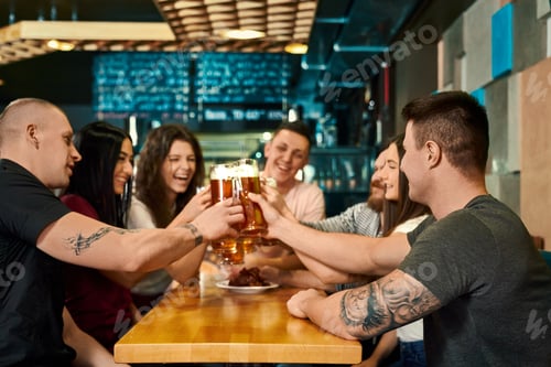 Preview: Young friends keeping pints with beer and toasting in pub