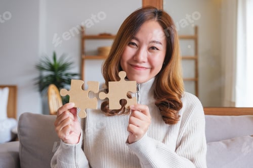 Preview: Portrait image of a woman holding and putting a piece of wooden jigsaw puzzle together
