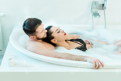 Preview: handsome man lying in bathtub with sexy brunette woman in lace bra