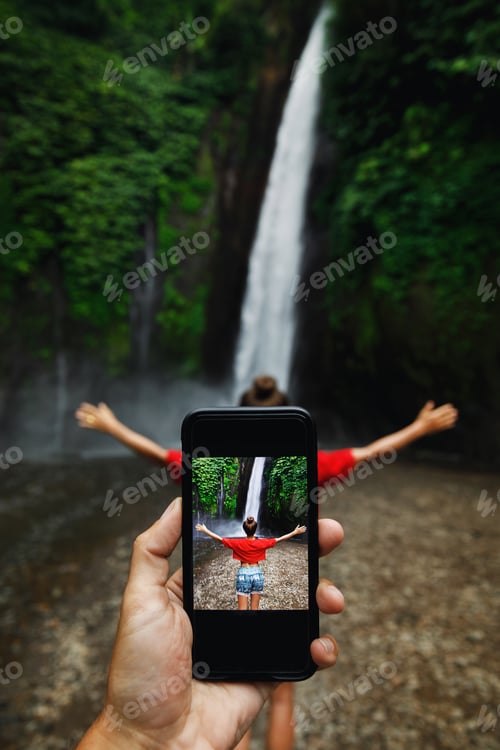 Preview: Man taking picture of her girlfriend beside beautiful waterfall