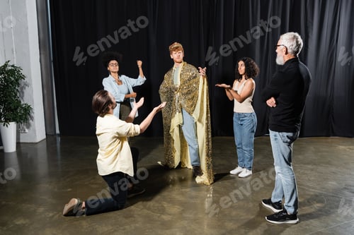 Preview: young man in king costume standing with outstretched hand near posing actors and grey haired art