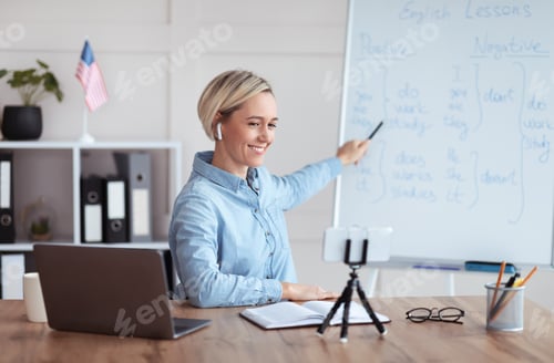 Preview: Happy female teacher giving online English lesson from home, pointing at blackboard, explaining