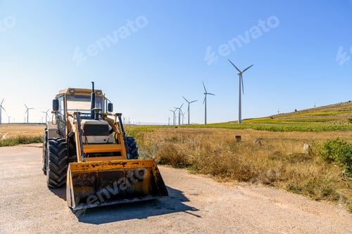 Preview: Excavator against wind turbines generating electricity on landscape of farmland