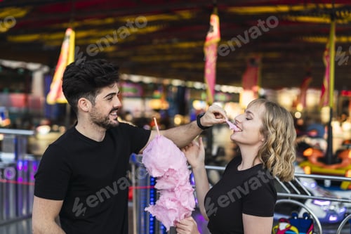 Preview: Young romantic couple eating cotton candy and having fun at an amusement park