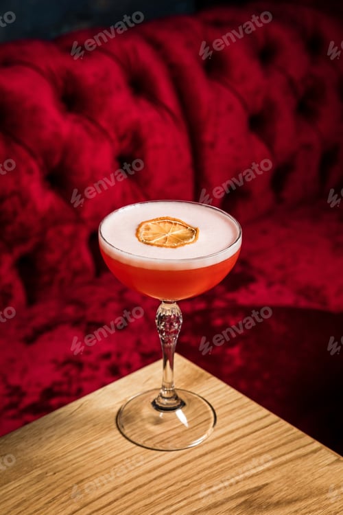 Vista previa: Un cóctel alcohólico de color rosa agrio con espuma adornado con una rodaja de limón seco, servido en una copa de cupé