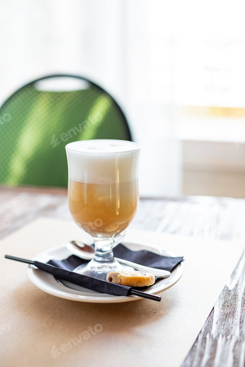 Preview: glass of Latte Macchiato with spoon, straw and plate with cookies on a wooden table.Delicious sweet