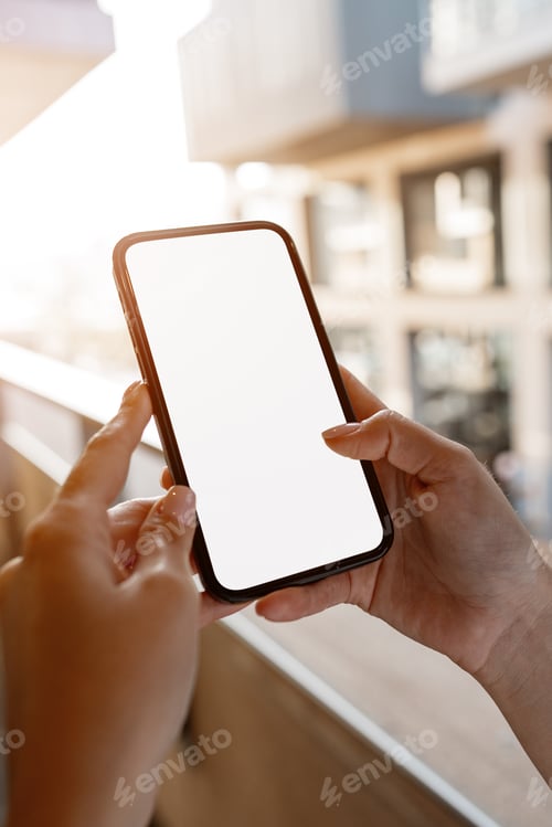 Preview: Hands holding a smartphone on a balcony during bright sunlight in a city setting