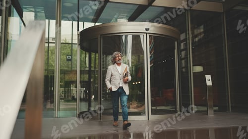 Preview: Mature businessman with beard in eyeglasses walks down the street past modern buildings