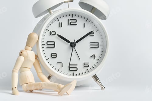 Vista previa: El hombre de madera se sienta cerca de un despertador blanco. El concepto de larga espera, fugacidad del tiempo, vejez.
