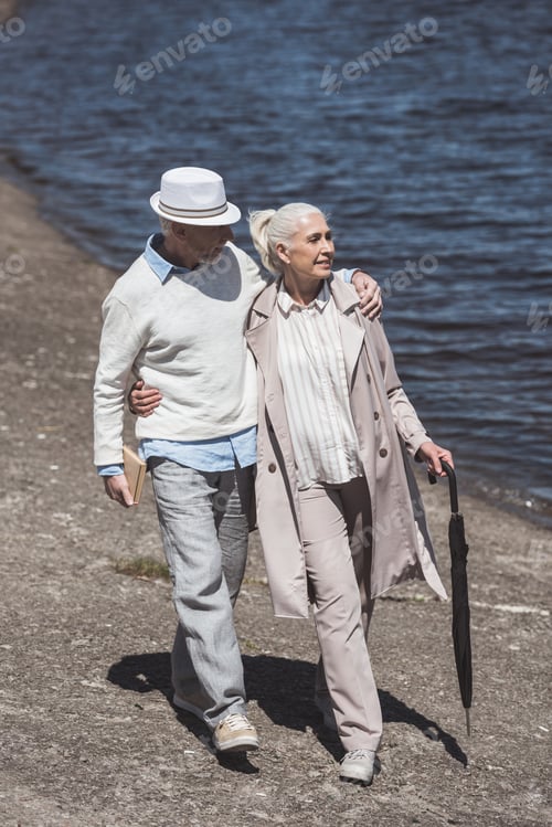 Preview: stylish senior couple walking on river shore at daytime