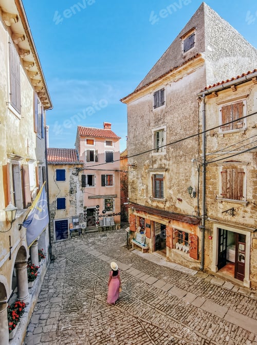 Preview: High angle view of woman in pink dress walking alone in square of picturesque old town