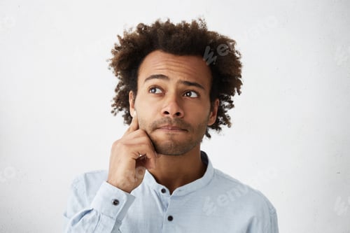 Preview: Close up portrait of forgetful and clueless dark-skinned student with stubble touching face, trying