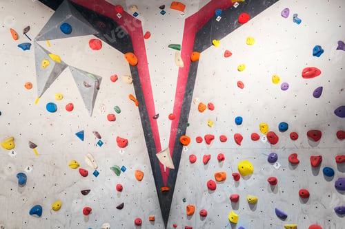 Preview: Grey wall with climbing holds and ropes in gym.