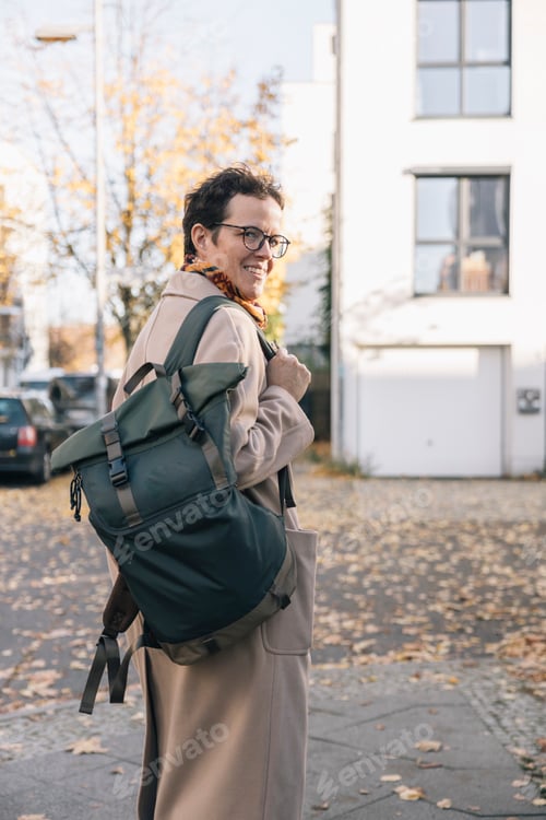 Preview: Smiling businessperson walking to work carrying backpack
