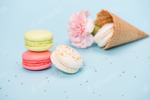 Preview: Group of handmade macarons in waffle cone and pink flower on blue surface. macarons background