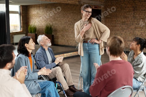 Preview: Grateful woman receiving applause from support group members during rehab therapy session