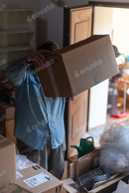 Preview: Person obscured by a big cardboard box in a cluttered storage area, depicting moving or organizing
