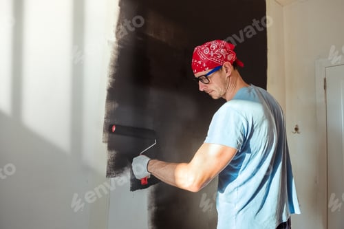Preview: Young man painting wall in black color, renovation home concept