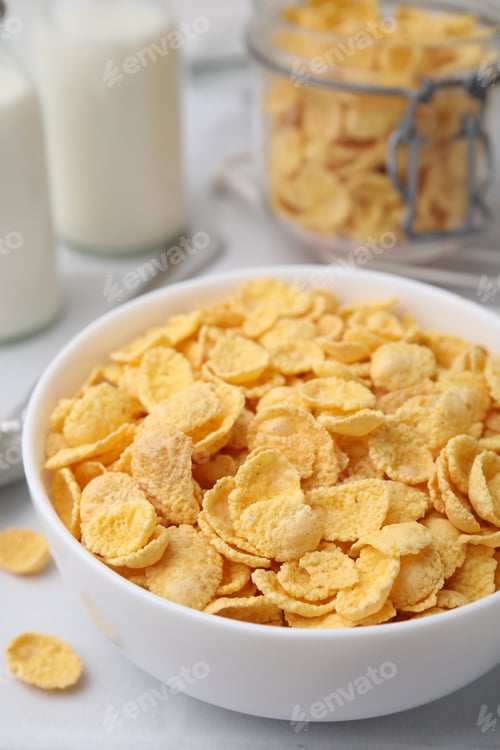 Preview: Tasty crispy corn flakes in bowl on white table, closeup. Breakfast cereal