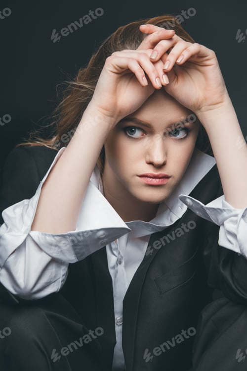 Preview: Young adult woman sitting and posing in male costume on black background, studio shot