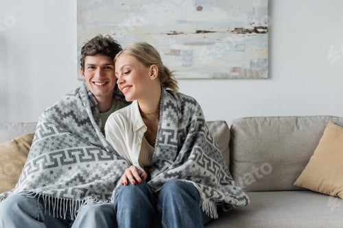 Preview: happy young man and woman covered in blanket sitting on couch