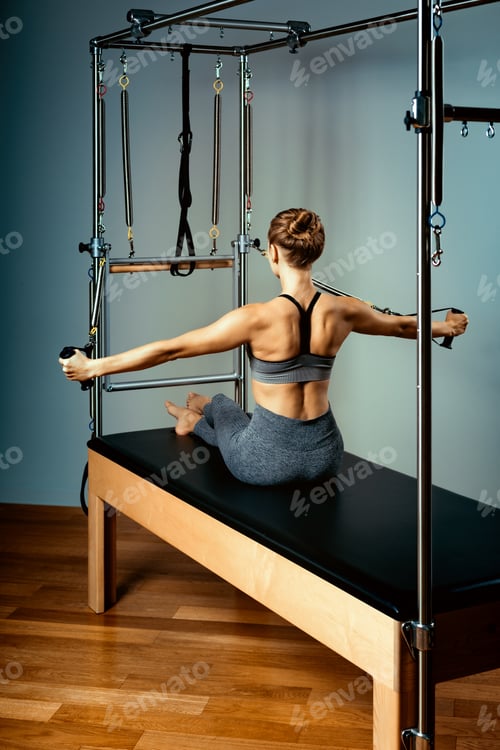 Preview: Gymnast woman pilates stretching sport in reformer bed instructor girl. Blue background, healthy