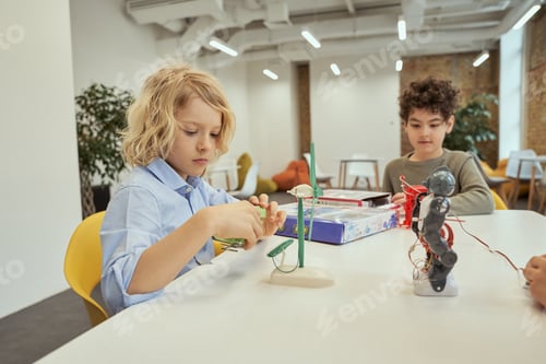 Preview: Curious caucasian boy examining technical toy full of details while sitting at the table together