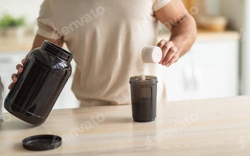 Preview: Cropped view of young fit guy making protein shake in kitchen, closeup