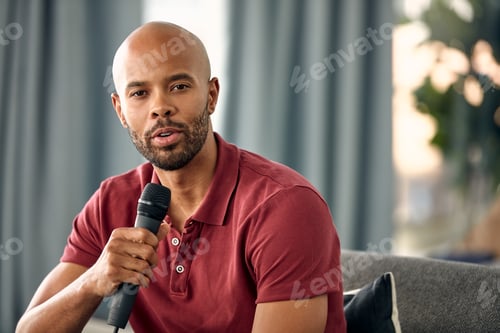 Preview: Cropped shot of a young man sitting on a sofa while speaking over a microphone