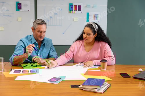 Preview: Multiracial businessman and businesswoman discussing strategy over documents in creative office