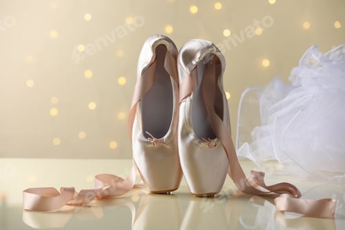 Preview: Pair of beautiful pointe shoes on beige background against blurred lights. Bokeh effect