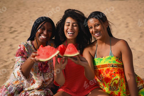 Preview: Happy group of multiracial women cheering with watermelon on the beach