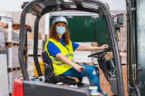Preview: Industrial female worker wearing a medical mask using a loader in a warehouse