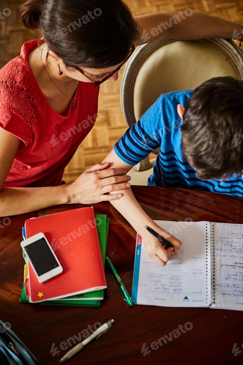 Preview: High angle view of mother at dining table helping son with homework