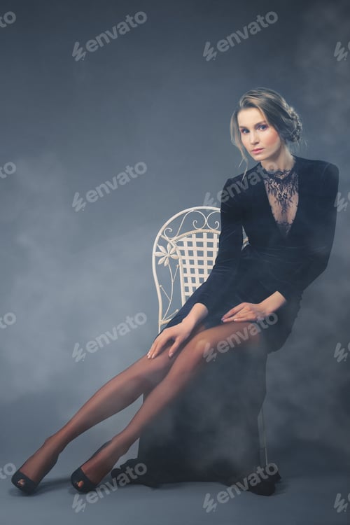 Preview: Beautiful lady in long velvet dress with deep cut sitting on chair
