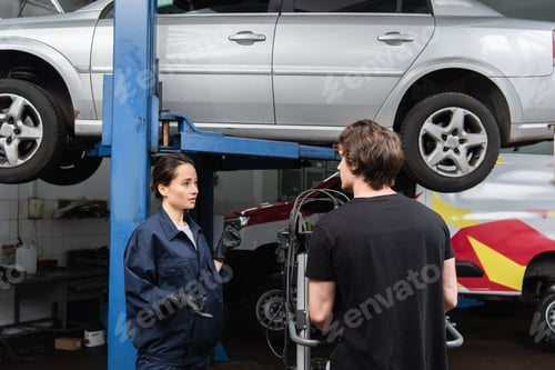 Preview: Workwoman pointing with fingers at car near colleague in garage
