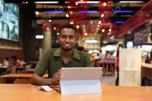 Preview: Portrait of handsome young black man using laptop computer in coffee shop