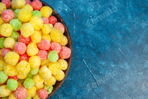 Preview: Half shot of delicious coloured sweets in a small brown pot on the right side on blue background