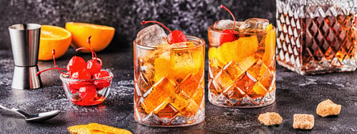 Preview: Old fashioned cocktail with cherries and orange twist.