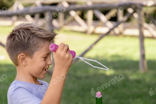 Preview: Happy kid boy blowing soap bubbles in a park