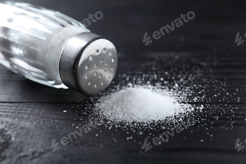 Preview: Organic salt in glass shaker on black wooden table, closeup