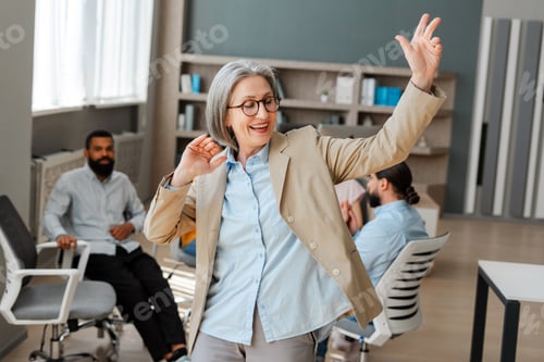 Preview: Happy senior businesswoman dancing in front of her team in modern office
