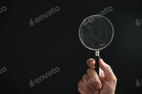 Preview: Hand holding a magnifying glass against a black background.