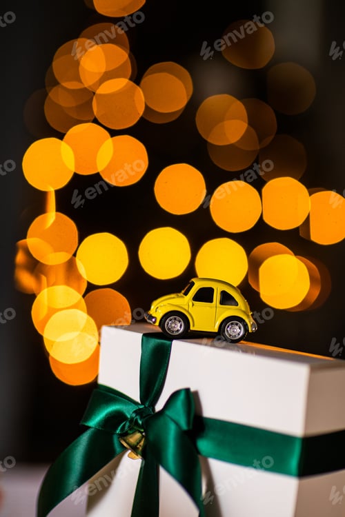 Preview: yellow small retro toy car on white gift with green ribbon on a Christmas yellow bokeh background