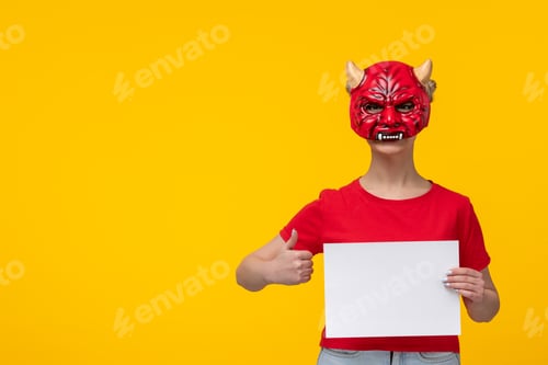 Preview: young female wearing scary devil mask holding piece of paper yellow background ugly