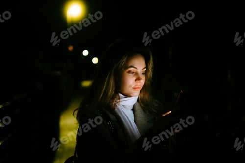 Preview: Young caucasian woman using mobile phone outdoor in the evening, walking on city streets.