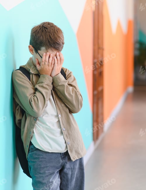 Preview: Sad schoolboy crying and covering his face at school hallway