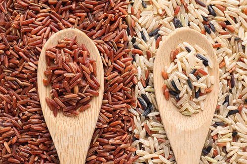 Preview: Pile of different brown rice with wooden spoons, flat lay