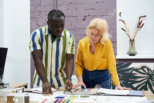 Preview: Creative designer pointing at blueprint and choosing colour with his colleague using palette at