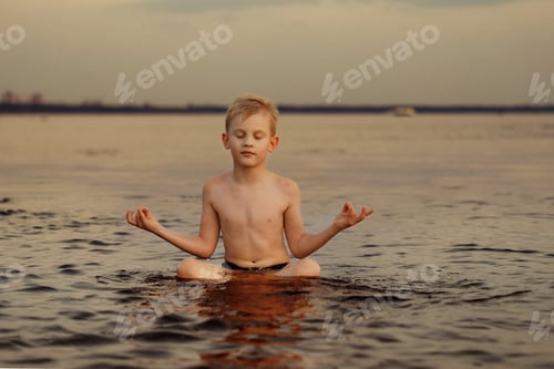 Preview: Cute Caucasian boy practicing meditation sitting in lotus position in the sea